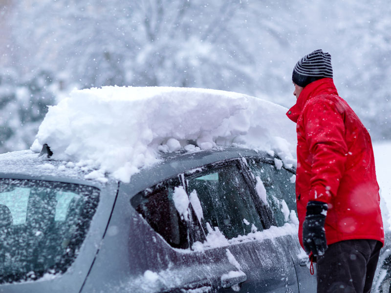 man cleaning snow on car